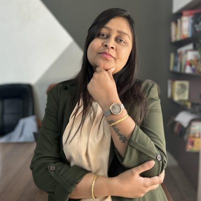 A woman in business attire with hand on chin, standing near bookshelf